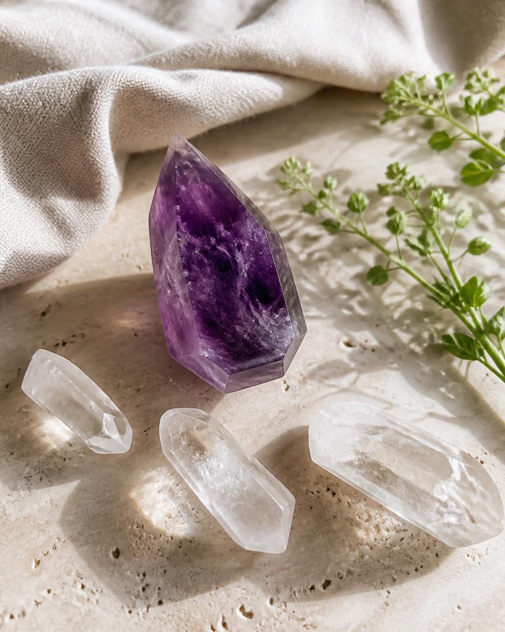 A polished amethyst point and clear quartz pieces on a travertine slab with linen