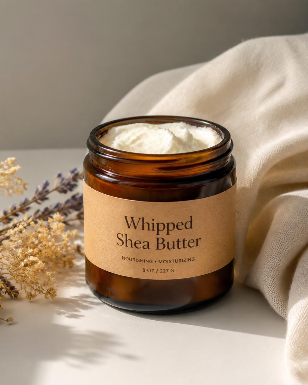 An amber jar of whipped shea butter with a kraft label beside soft linen and botanicals